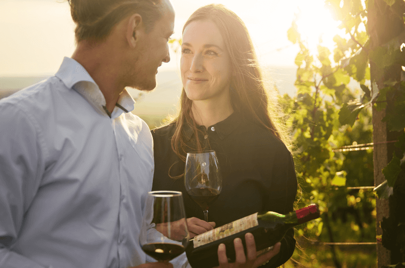 Muž a žena mezi vinohrady drží sklenku červeného vína a láhev archivního vína