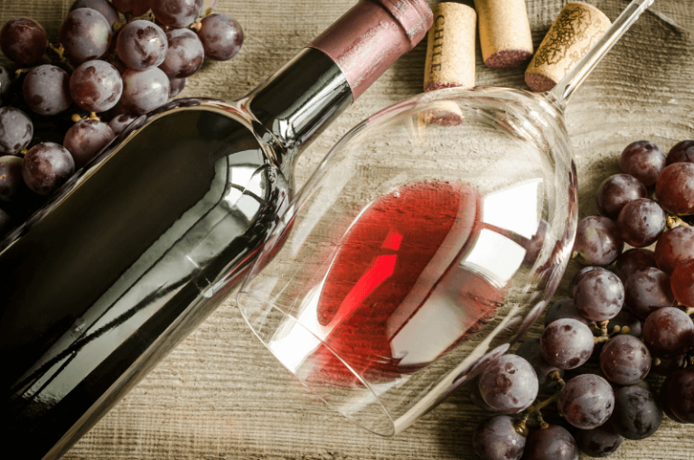 láhev červeného vína se sklenkou s červeným vínem položená na stole