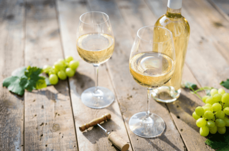dvě skleničky bílého vína na stole s trhy vinné révy