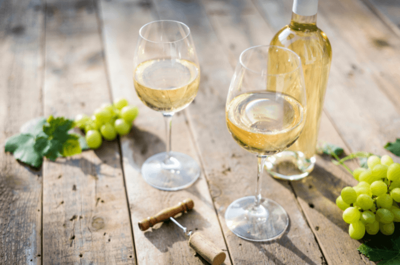 dvě skleničky bílého vína na stole s trhy vinné révy
