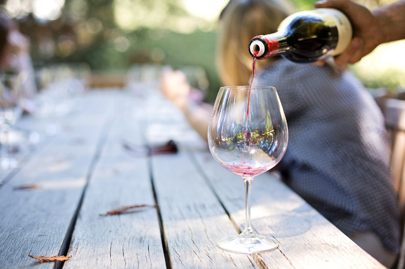 ruka rozlévá červené víno do skleničky na venkovním posezení