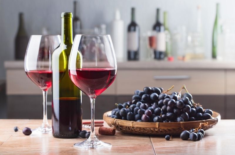butelka wina i dwa kieliszki czerwonego wina obok kiście winogron